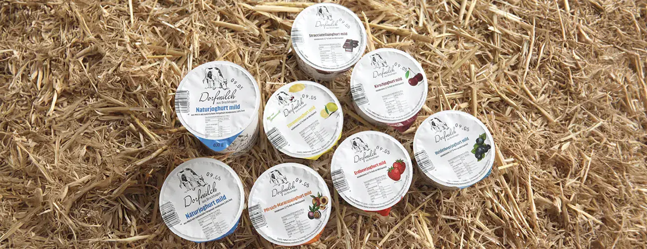 Dorfmilch-Joghurt in verschiedenen Sorten stehen auf Stroh
